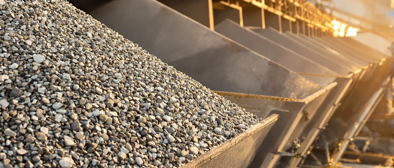 Aerial view of an asphalt plant at golden hour with dump trucks lined up on the access road