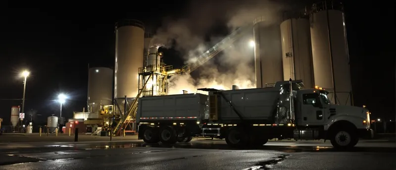 Hot mix asphalt loading into a dump truck under floodlights at night