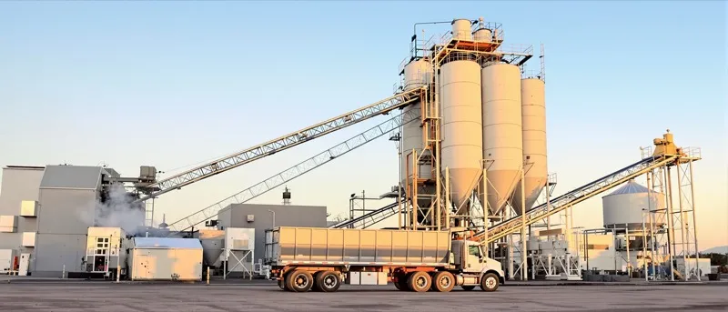 Unmarked dump truck under an asphalt plant silo loadout chute at sunrise