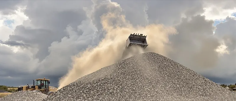 Front loader scooping aggregate from a stockpile under summer thunderclouds