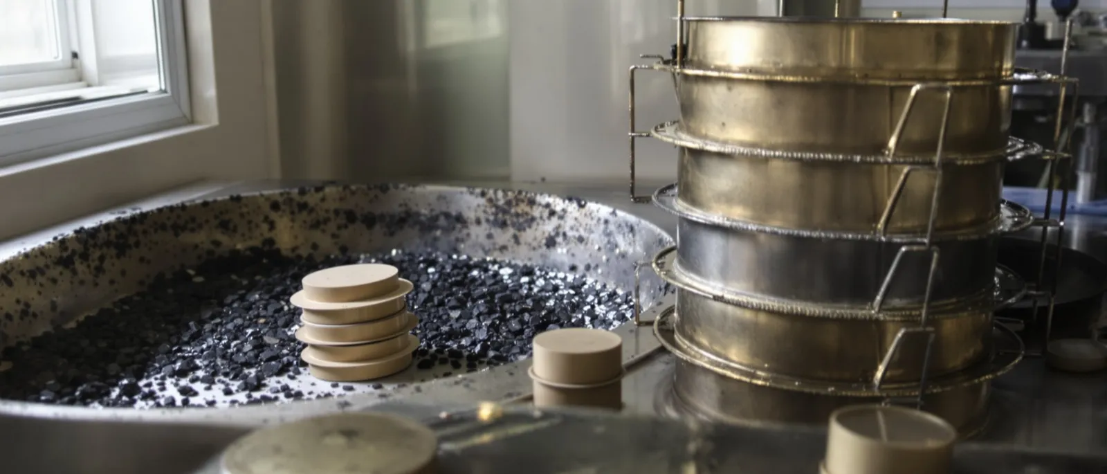 Asphalt mix samples, sieves and compacted specimens on a quality control lab bench