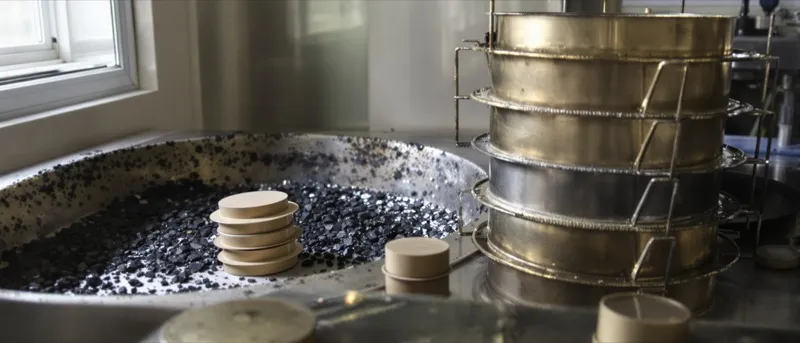 Asphalt mix samples, sieves and compacted specimens on a quality control lab bench