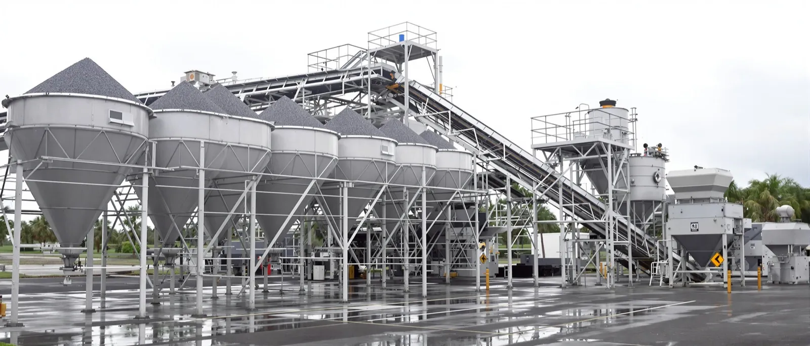 Aggregate cold feed bins and conveyor belt at an asphalt plant under overcast sky